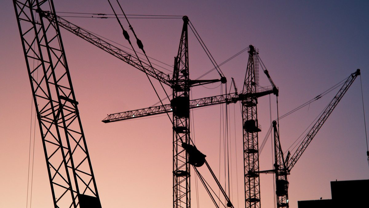 Several tower cranes silhouetted against a pink and purple dusk sky.