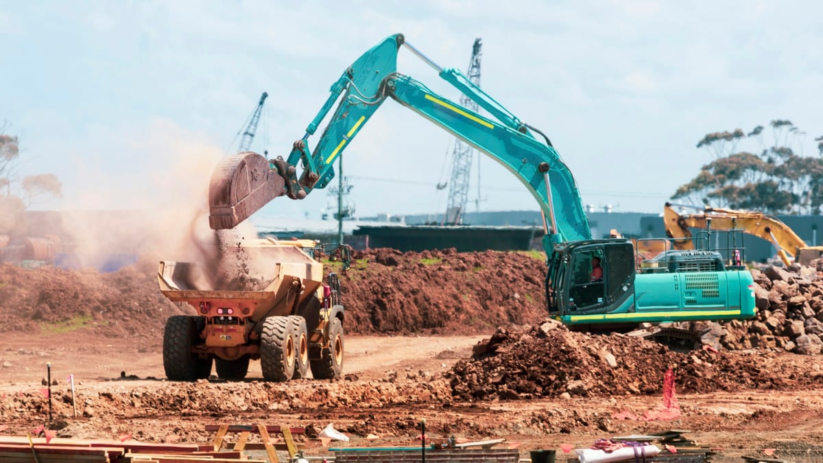 A tracked excavator loading loose earth into an articulated dump truck on a large open earthworks site.