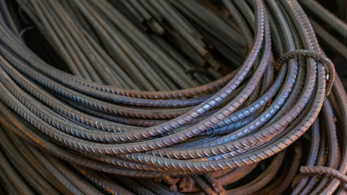 A close-up of tightly coiled steel reinforcing bar, the ridged rods overlapping in rusted bundles.