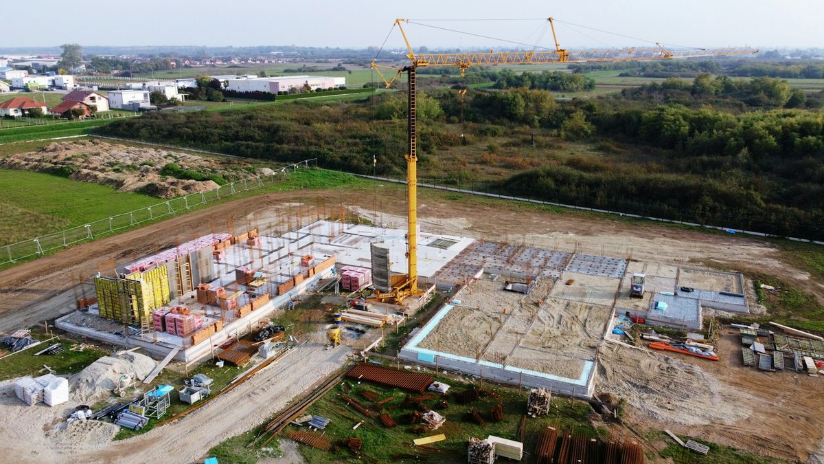 Elevated view of an active construction site with a tower crane, concrete foundations, formwork and stacked building materials.