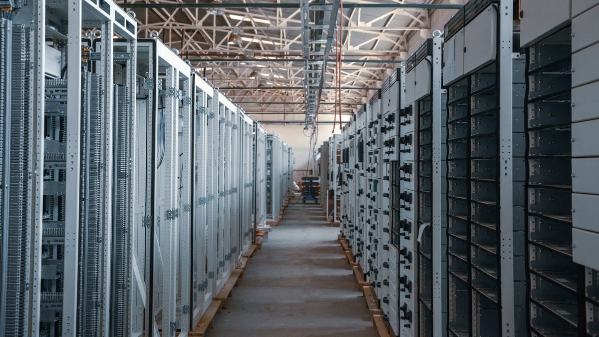 An aisle between rows of tall electrical equipment cabinets inside an industrial hall.