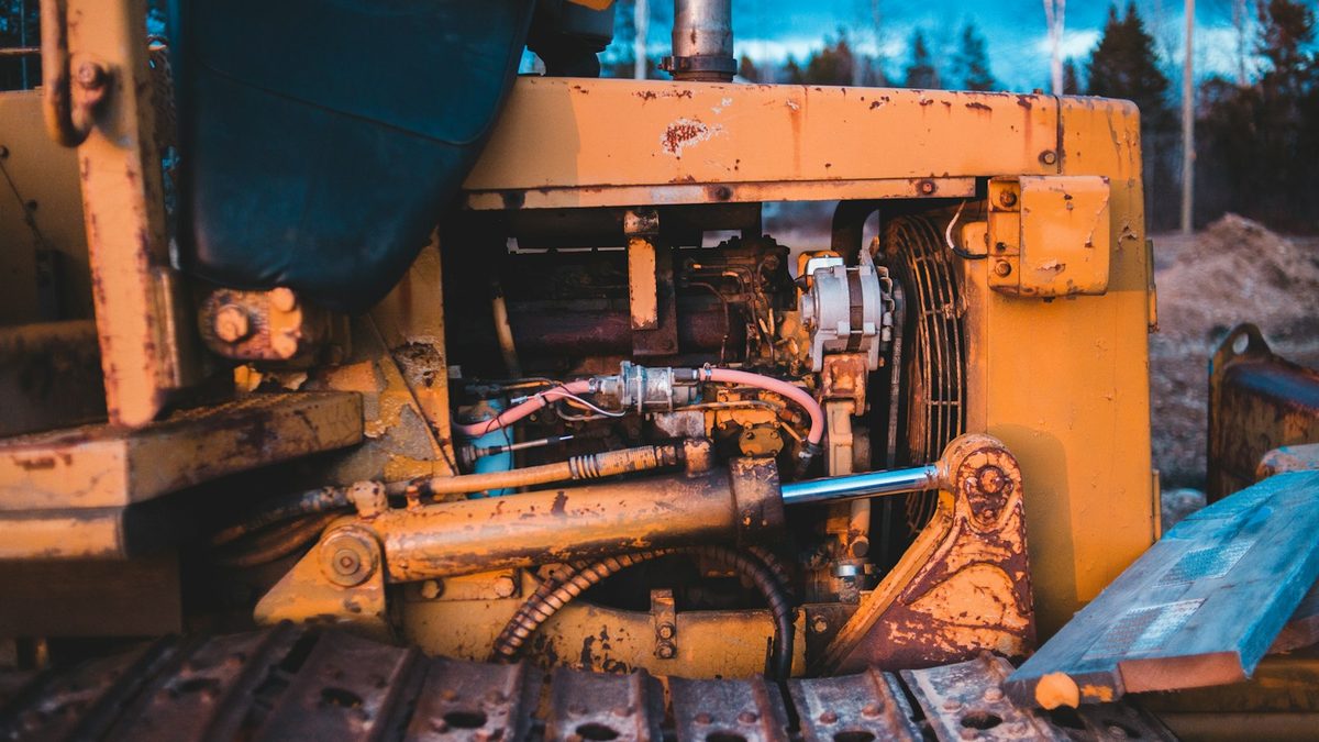 A close-up of a weathered yellow tracked bulldozer, showing its exposed engine bay, hydraulic rams and steel track plates.