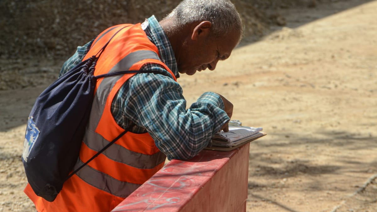 A construction worker in a high-visibility vest filling in paperwork resting on a low wall at a site.