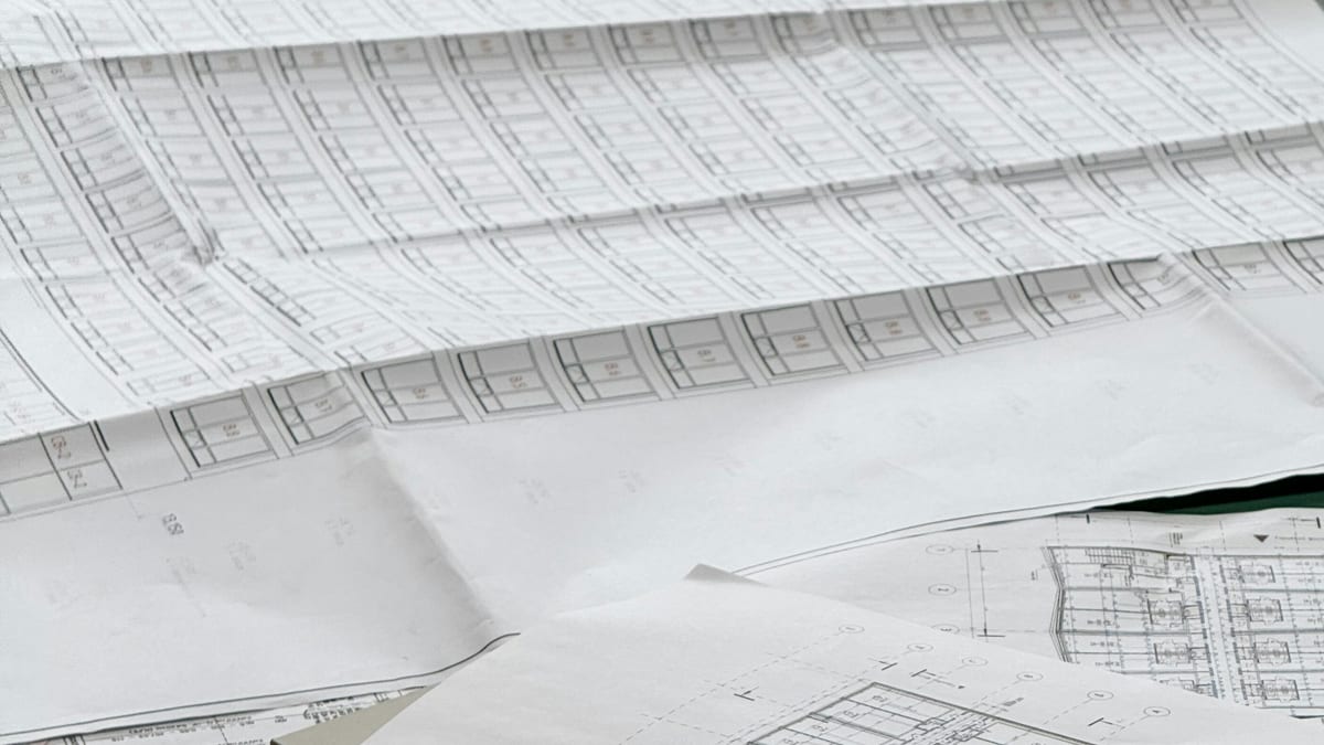Overlapping printed architectural floor plan sheets spread across a table.