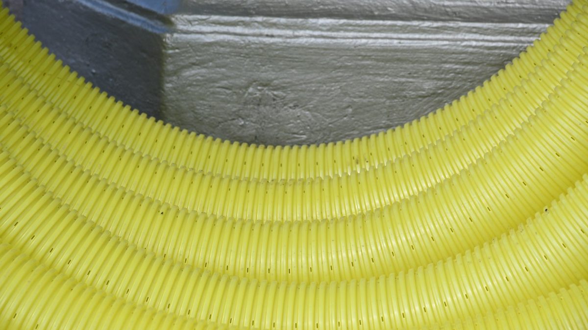 Coils of yellow corrugated flexible conduit curving around a grey concrete corner.