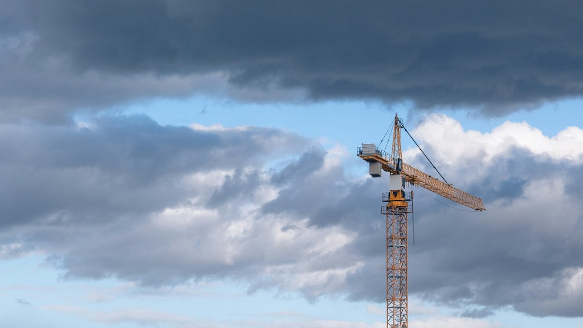 A yellow tower crane standing against a sky of heavy grey cloud broken by patches of blue.