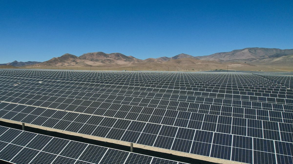 Rows of ground-mounted solar panels stretching toward arid hills under a clear sky.