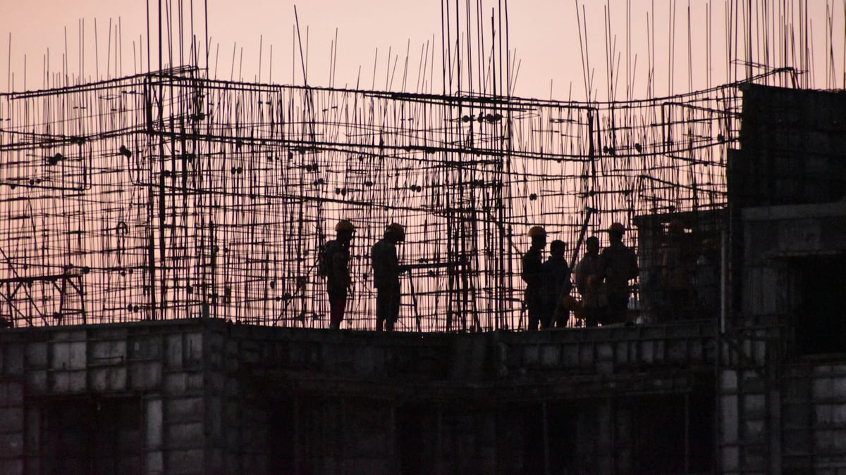 Silhouettes of a construction crew standing on a concrete slab among a dense forest of upright reinforcing bar at dusk.