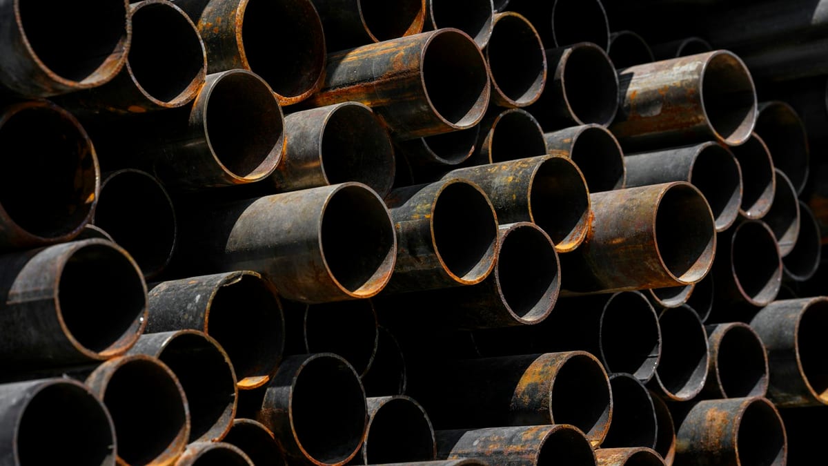 A close-up of a large stack of rusted black steel pipes, their open circular ends facing the camera in shadow.