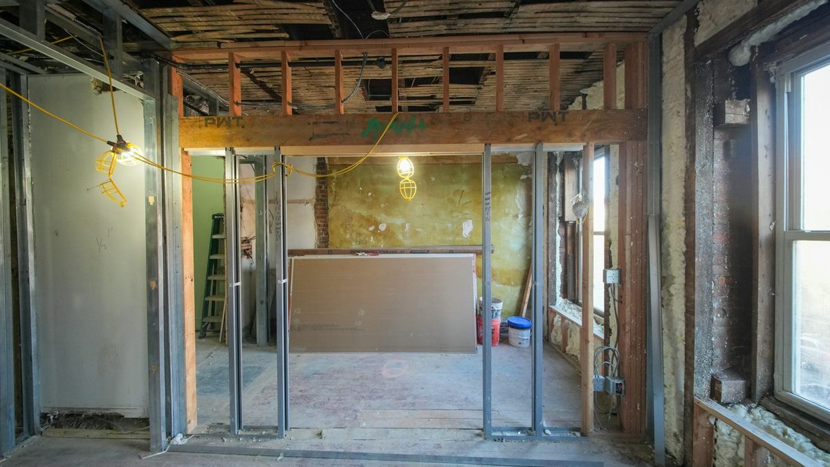 The stripped interior of a building mid-renovation: metal stud partitions, exposed ceiling joists, insulation at the windows and a sheet of drywall waiting to be hung.