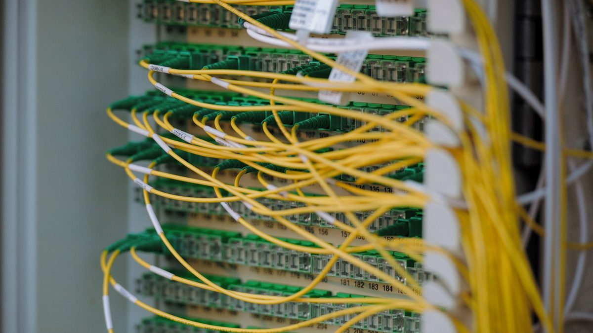 Yellow and green fibre-optic patch cables running across a numbered green termination panel inside an equipment rack.