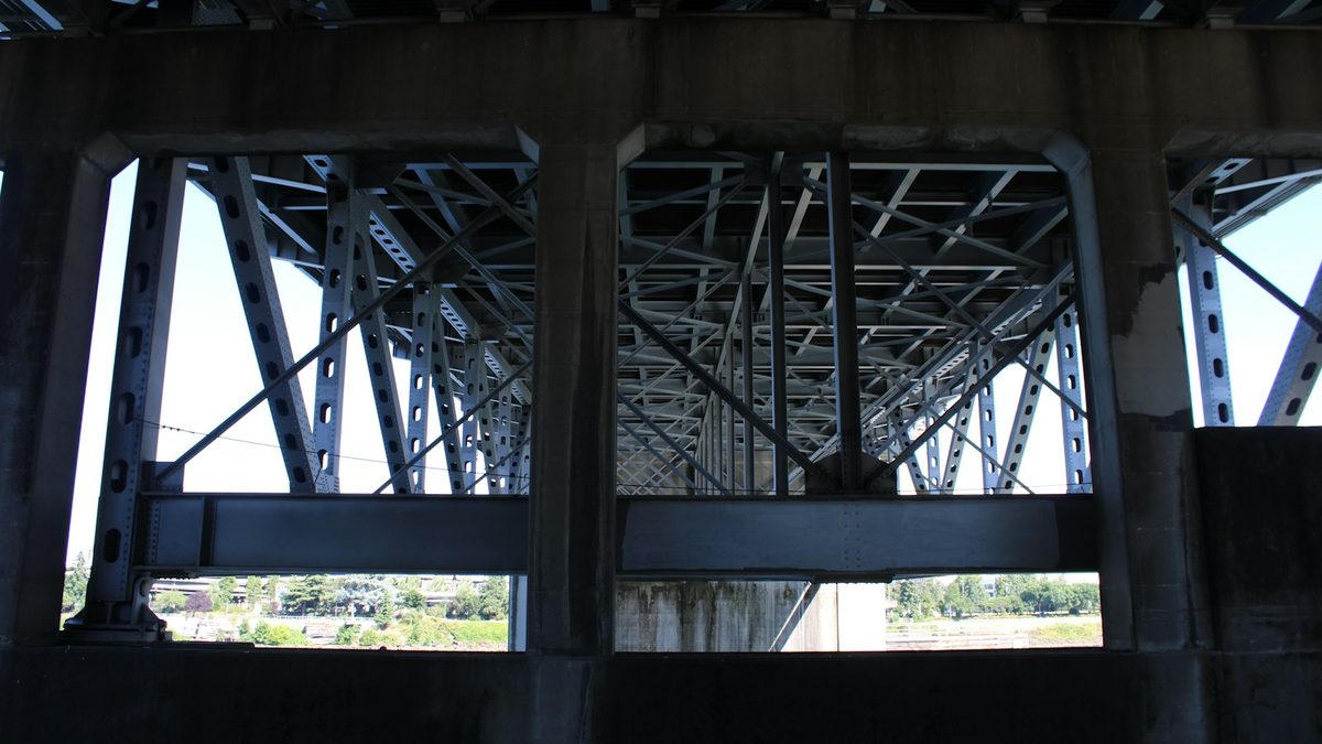 Steel truss girders and concrete piers seen from underneath a road bridge