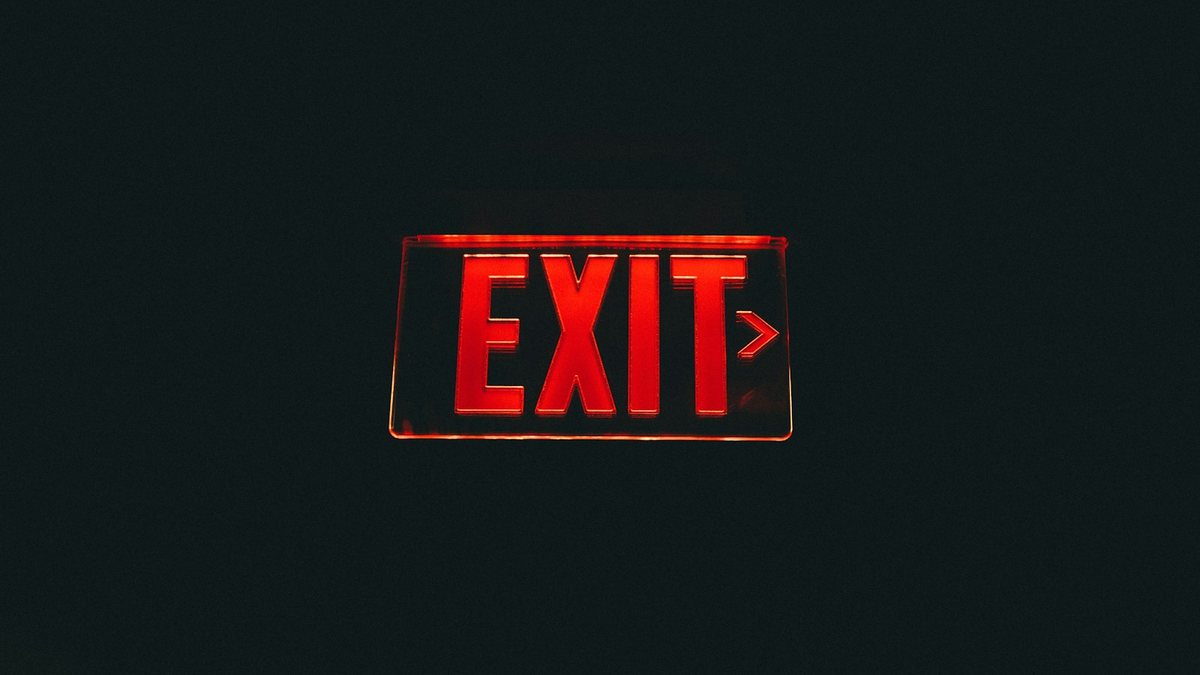 A red illuminated EXIT sign with a right-pointing arrow glowing against a dark wall.