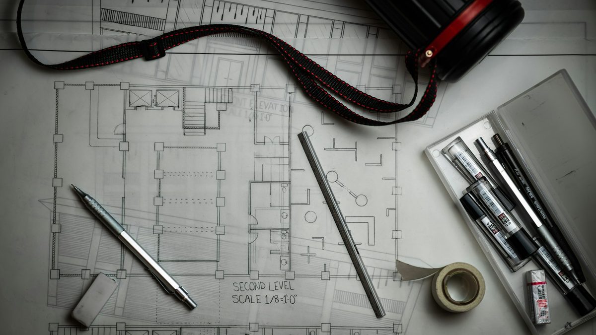 An architectural floor plan on a desk with drafting pencils, an eraser and a drawing tube