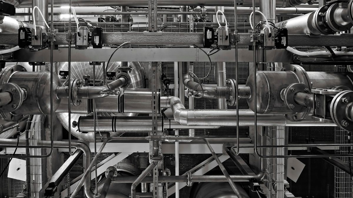 A dense arrangement of stainless steel pipework, flanges, valves and mounted instrumentation inside a building's mechanical plant room.