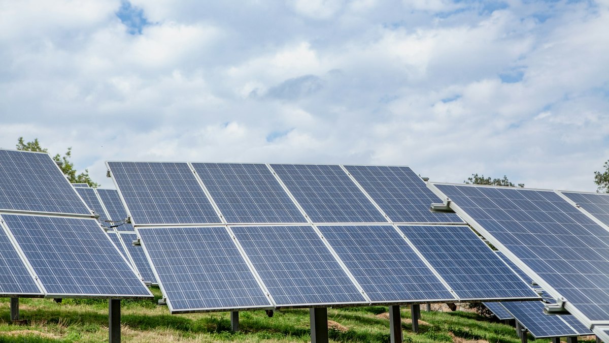 Rows of ground-mounted solar panels on steel posts in a grassy field.